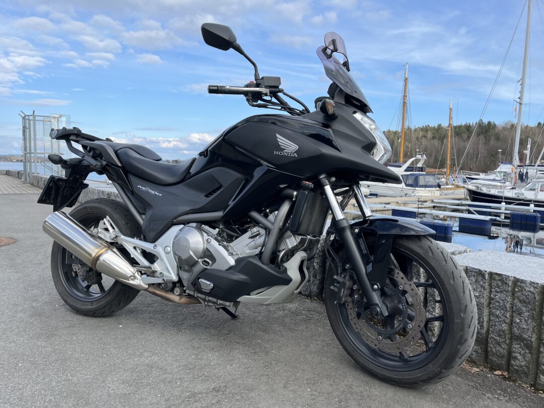 Black Honda motorcycle parked on a waterfront promenade with boats in the marina behind it.