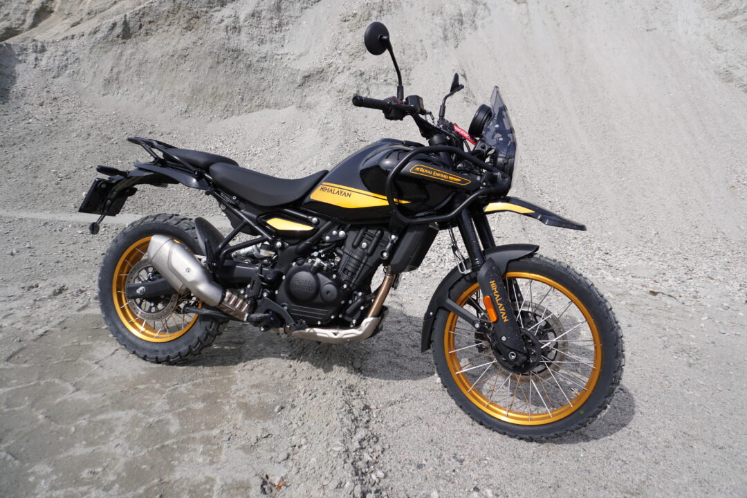 Black Royal Enfield Himalayan motorcycle with yellow accents parked on a gravel surface.