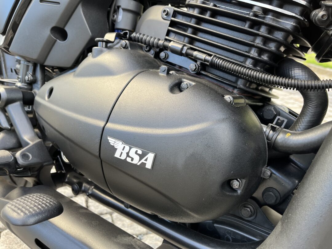 Close-up of a black motorcycle engine and frame with bolts, hoses, and a BSA emblem on the side cover.